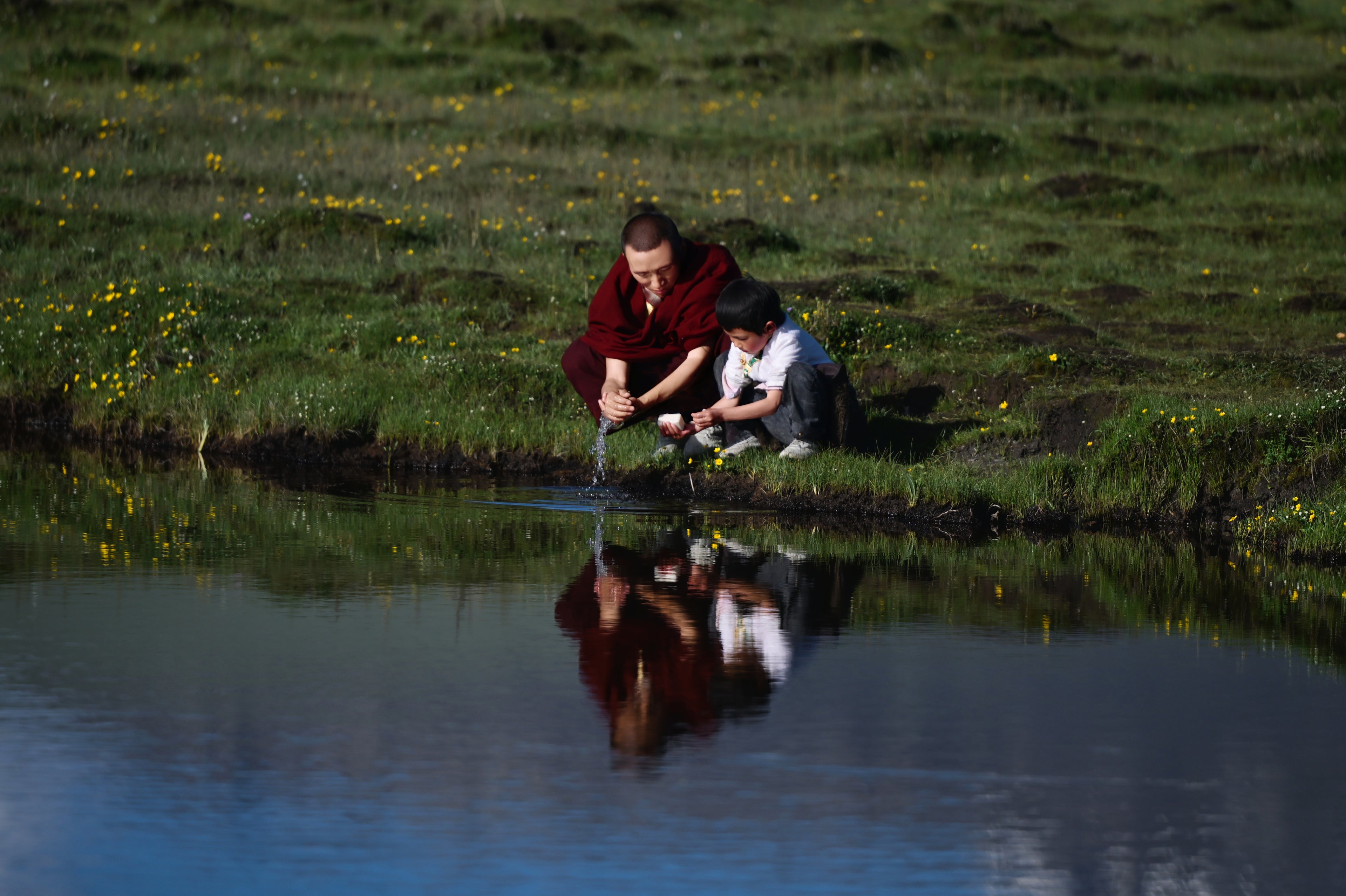 A Tibetan monk and a Tibetan kid are washing hands together with Tsoji handmade all natural soap and water from a mountain lake